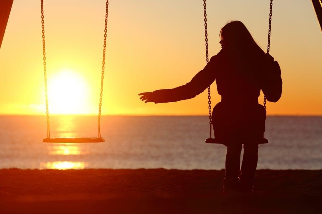 Woman-reaching-for-empty-swing-at-sunset